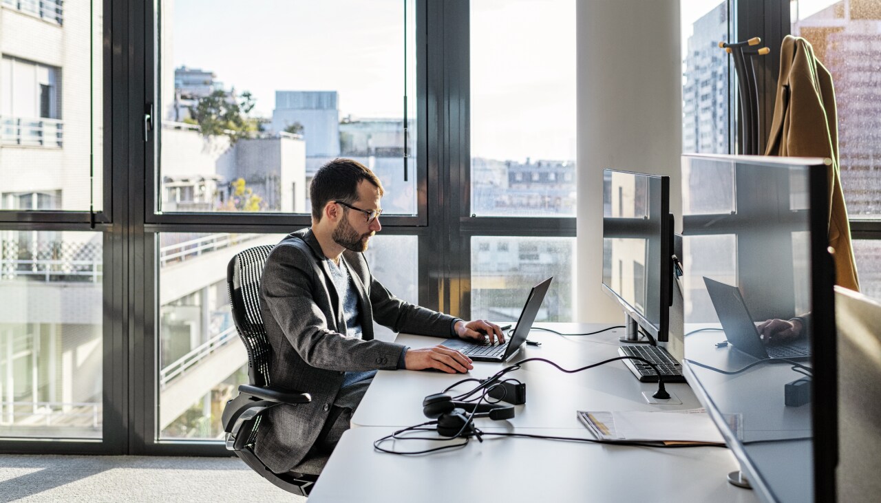Ein Mann sitzt in einem Büro mit Glasfassade an seinem Laptop